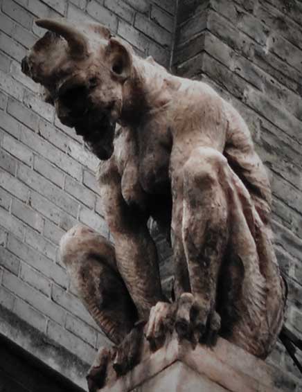 A stone devil looking down from a City roof top.